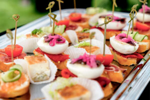 A platter of assorted hors d'oeuvres featuring bite-sized pieces topped with vegetables, garnishes, and skewers. The colorful presentation includes tomatoes, pickled onions, and layers of different ingredients, suitable for Catering Riesa.